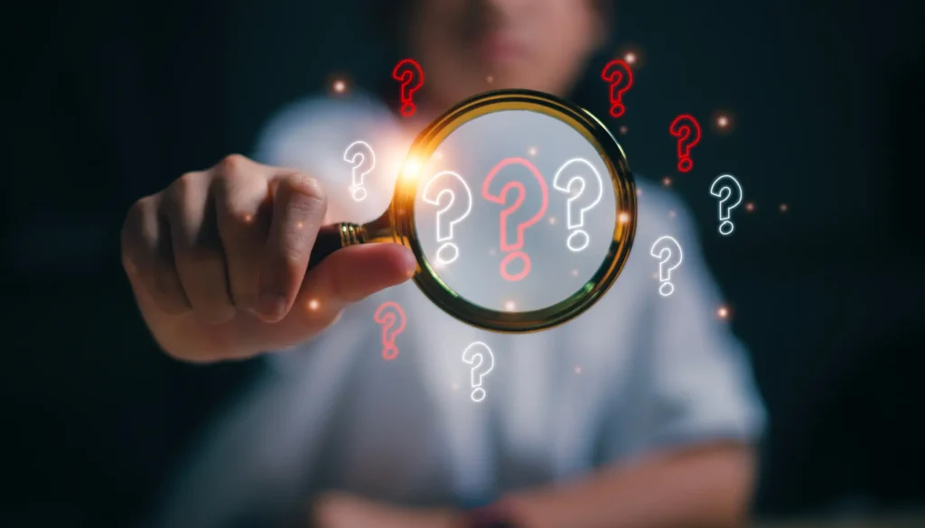 Close-up of a magnifying glass surrounded by numerous small question marks, symbolizing curiosity, investigation, and the search for answers.