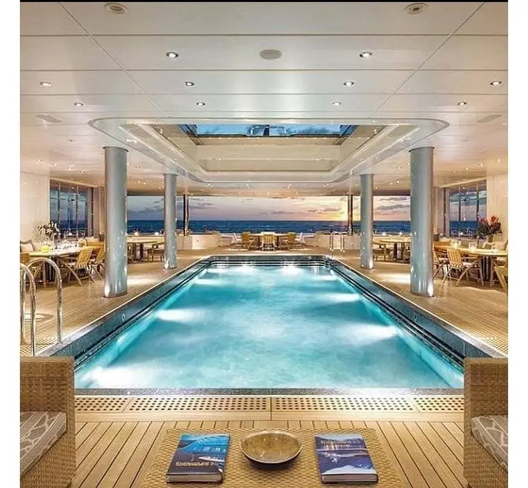 Luxury indoor swimming pool area inside a superyacht with panoramic ocean views at sunset