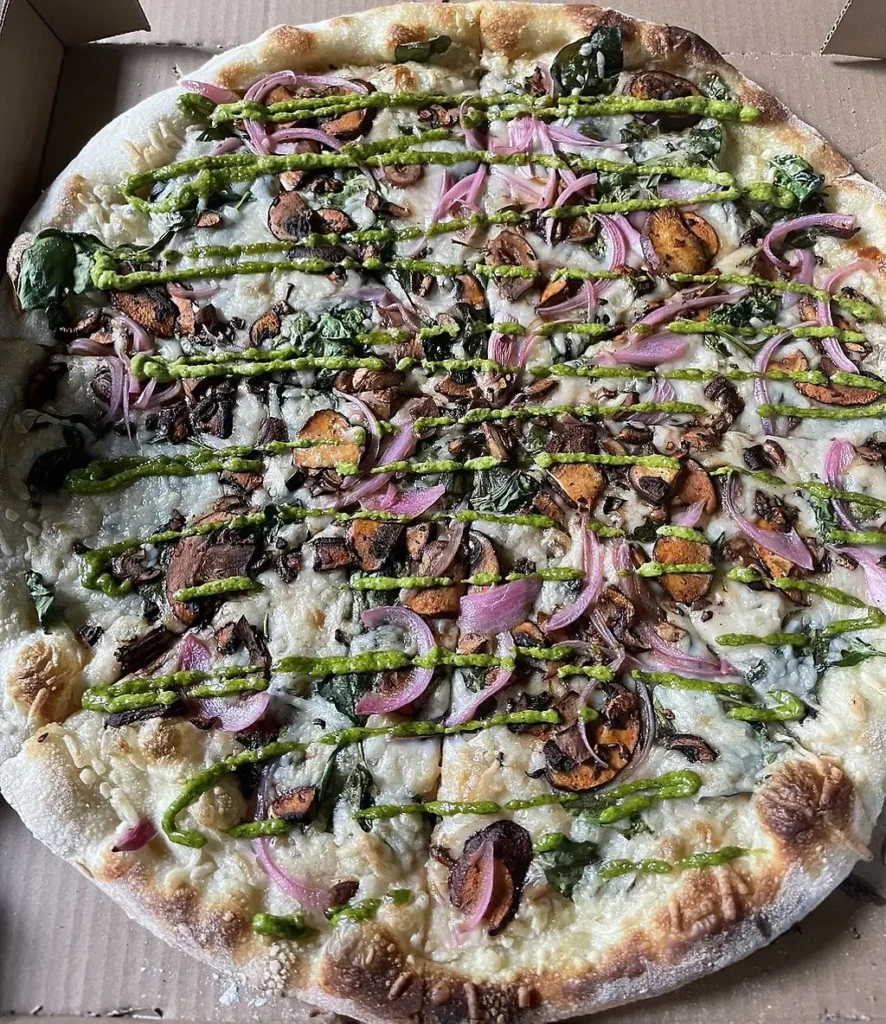 Thin crust sourdough pizza with mushrooms, red onions, spinach, and pesto drizzle from Nick's Pizza Oakland